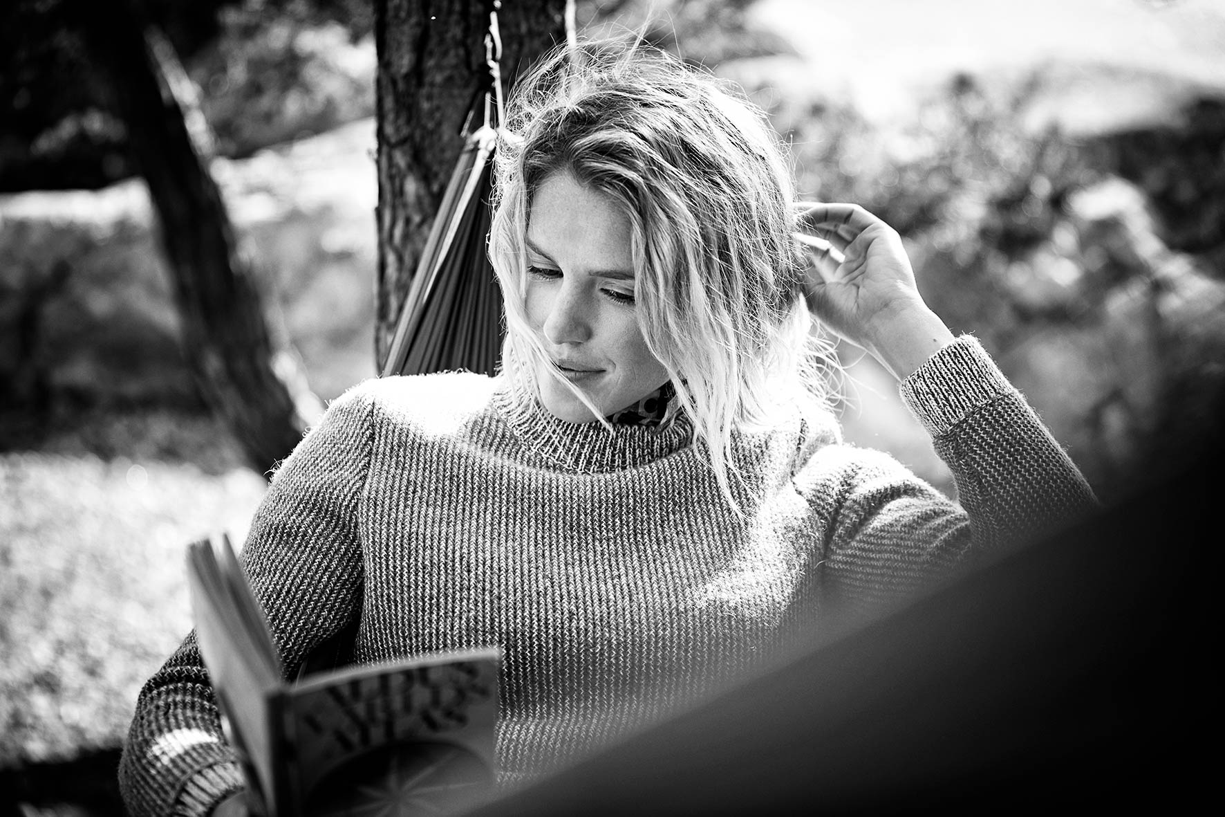 Woman wearing a fair fashion jersey by Hess Natur, lying in a hammock reading a book in nature.