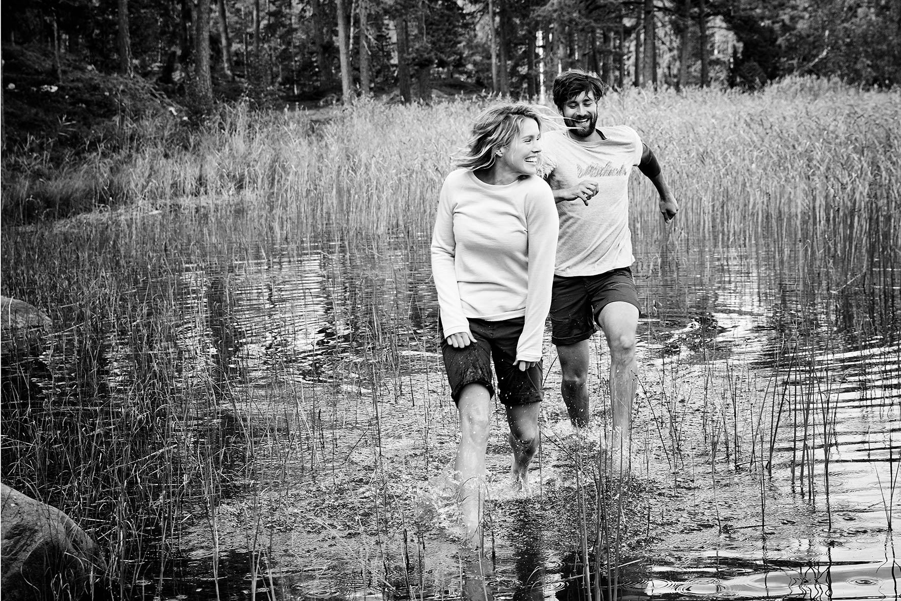 Black and white photo of a couple wearing fair fashion clothes while jumping barefoot through a lake near Stockholm, Sweden.